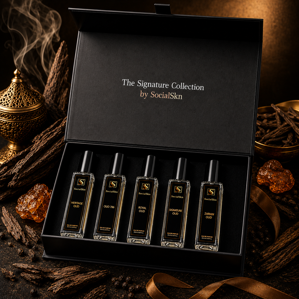 A luxury gift set containing five  glass perfume bottles with black caps, presented in an open black box. The box lid features the gold text 'The Signature Collection by SocialSkn'.